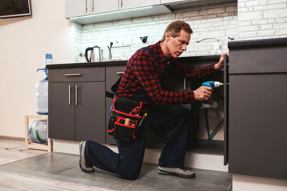 A tradesman drilling inside a base cabinet